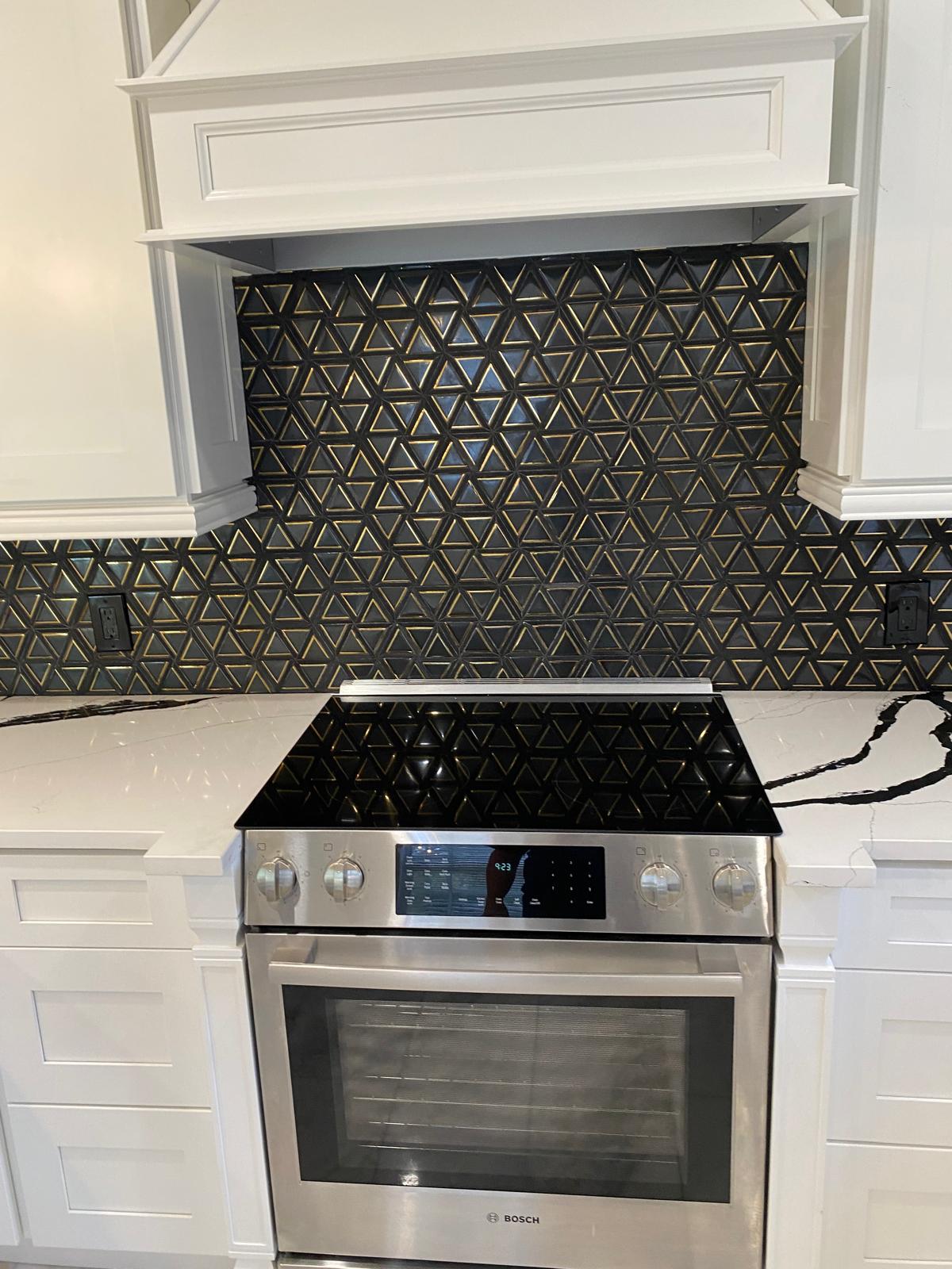 Black and gold triangular glass mosaic backsplash behind a slide-in range with quartz counters