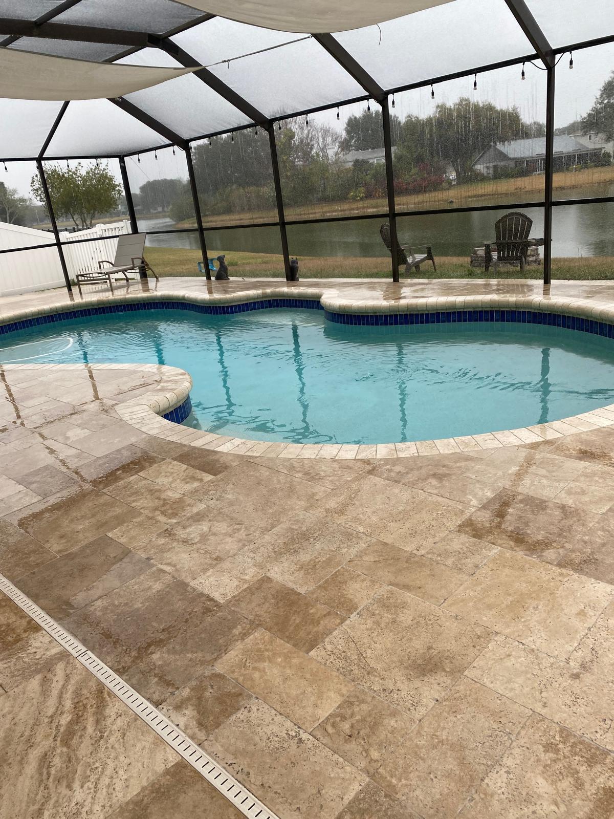 Travertine paver pool deck in a screened Tampa lanai with blue glass waterline tile
