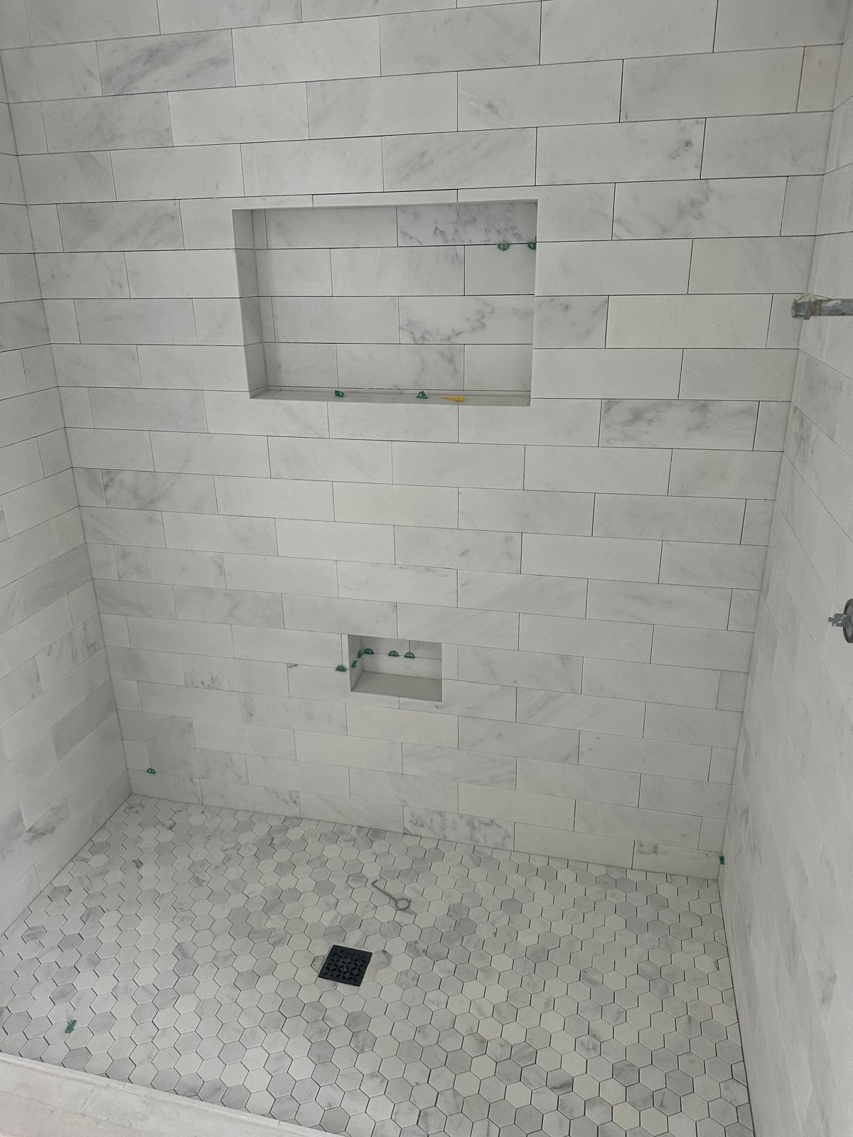 Carrara marble subway shower with twin niches and a hand-cut hex pan